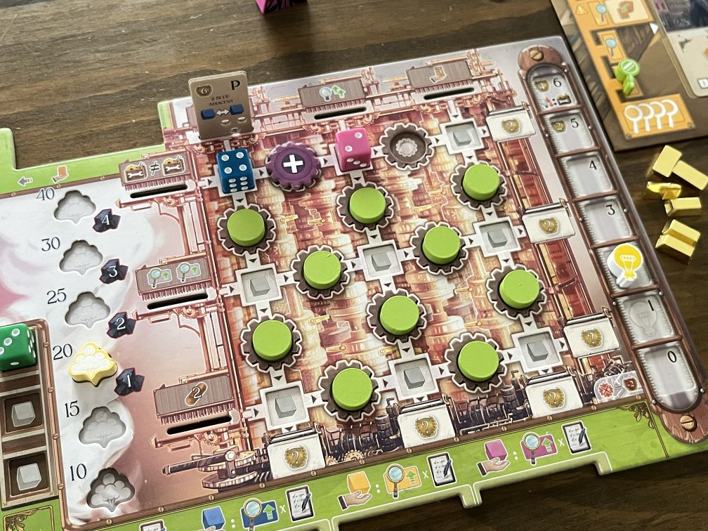 Das Bild zeigt einen weiteren Ausschnitt aus dem Brettspiel Ada's Dream. Im Mittelpunkt steht das Spielfeld "Ada's Study", auf dem Zahnräder und Marker in einem 3x3-Raster angeordnet sind. Auf den Zahnrädern sind verschiedene Spielsteine in Grüntönen platziert, die mit Würfeln in Blau und Pink sowie speziellen Symbolen (wie einem Pluszeichen) kombiniert sind. Am oberen Rand des Spielfeldes befindet sich eine Fortschrittsanzeige, die den aktuellen Stand im Spiel darstellt. Links sind grüne Würfel und Wolkenmarker sichtbar, die auf den Fortschritt in verschiedenen Bereichen des Spiels hinweisen. Rechts vom Spielfeld sieht man einige Ressourcenmarker in Form von Kupferbarren. Die Farben und Details der Spielkomponenten sind lebendig und tragen zur komplexen Spielmechanik bei.